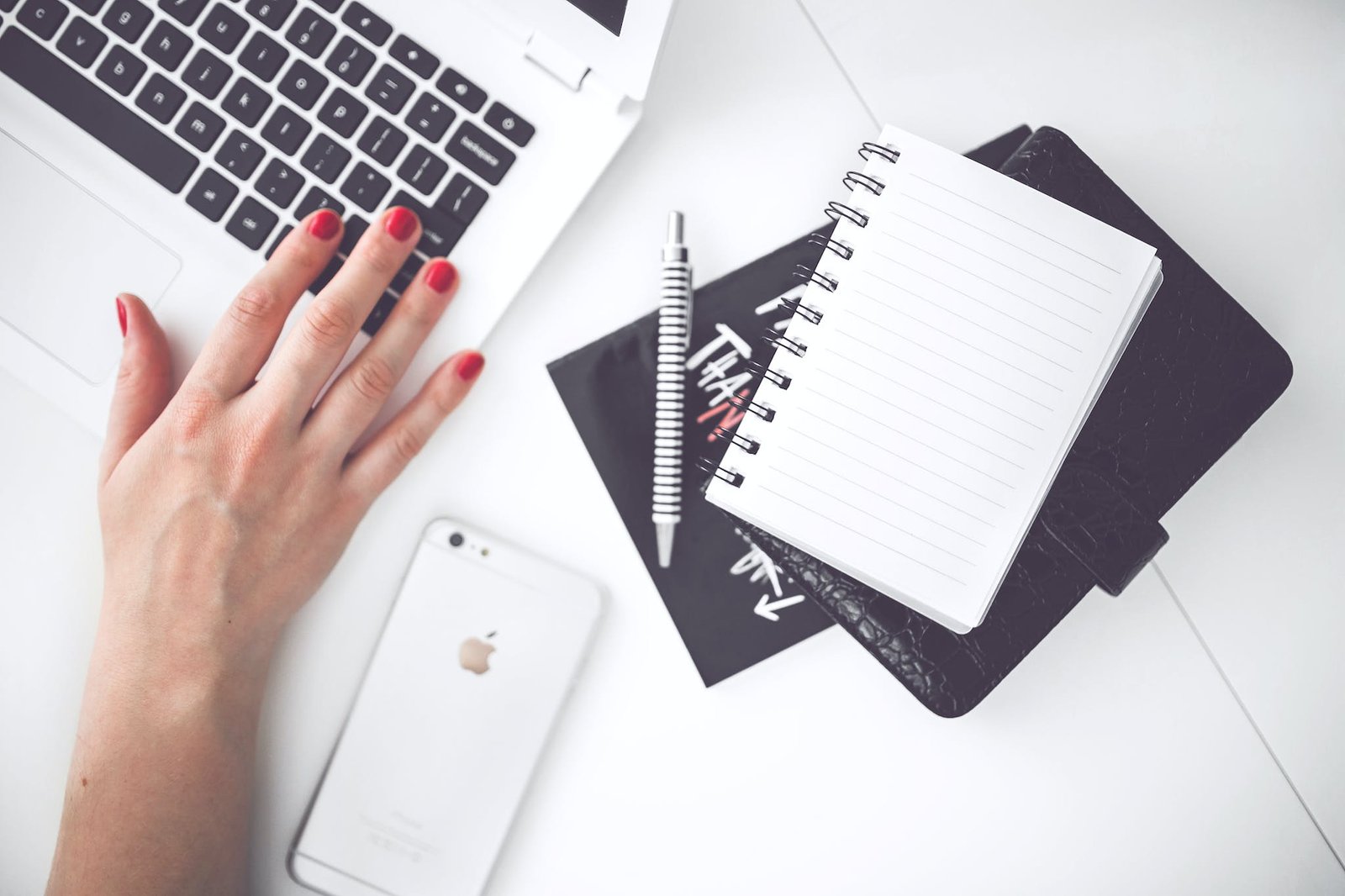 White laptop, female hand, note, pen, phone, desk